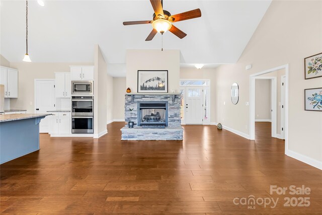 unfurnished living room featuring ceiling fan, dark hardwood / wood-style floors, high vaulted ceiling, and a stone fireplace