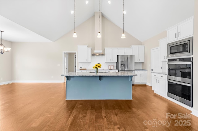 kitchen with pendant lighting, white cabinetry, stainless steel appliances, light stone countertops, and an island with sink