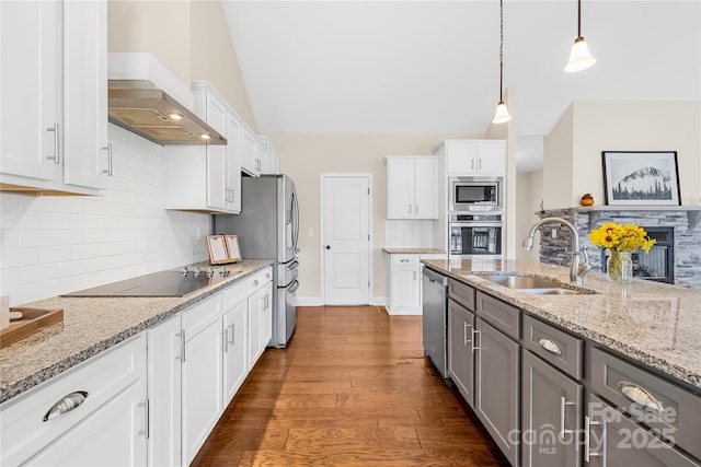 kitchen with sink, white cabinetry, hanging light fixtures, appliances with stainless steel finishes, and wall chimney range hood