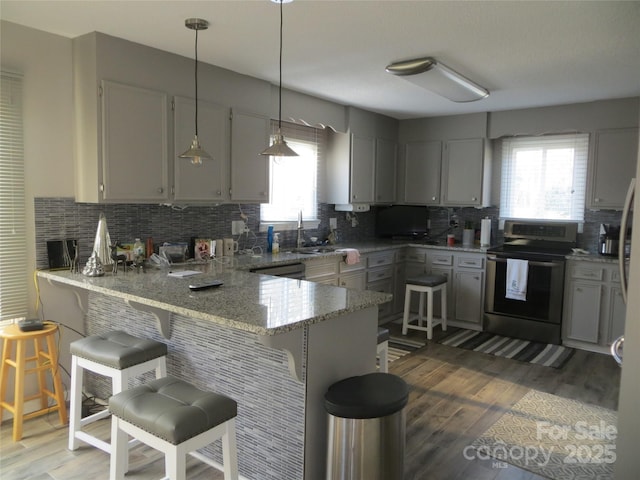 kitchen with hanging light fixtures, gray cabinets, electric range, and kitchen peninsula