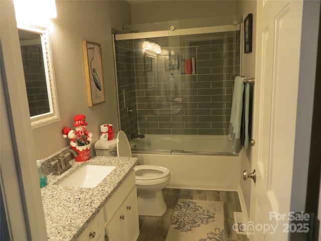 full bathroom featuring hardwood / wood-style flooring, bath / shower combo with glass door, vanity, and toilet