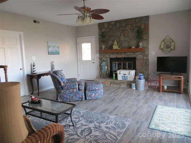 living room featuring wood-type flooring, a stone fireplace, and ceiling fan