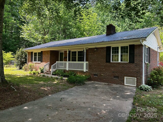 ranch-style house featuring covered porch, a chimney, brick siding, crawl space, and metal roof