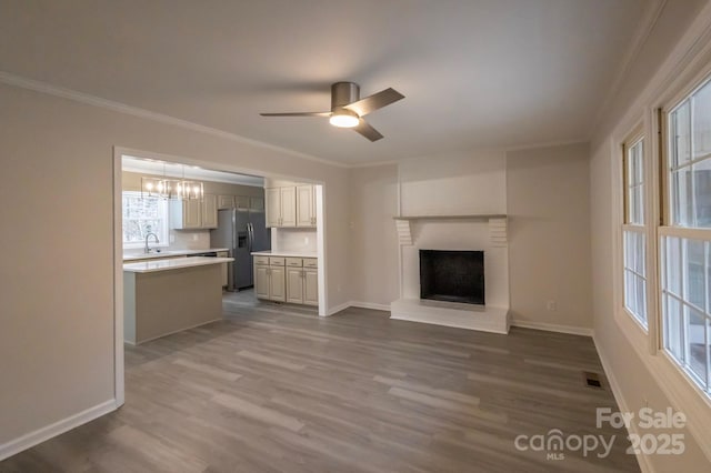 unfurnished living room featuring visible vents, crown molding, baseboards, dark wood-type flooring, and ceiling fan with notable chandelier