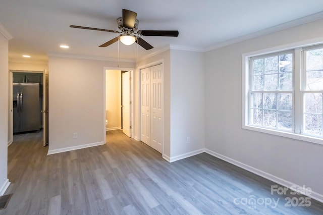 unfurnished bedroom with crown molding, a closet, wood finished floors, baseboards, and stainless steel refrigerator with ice dispenser