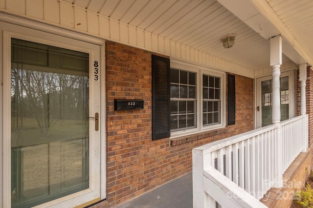 view of exterior entry featuring covered porch and brick siding