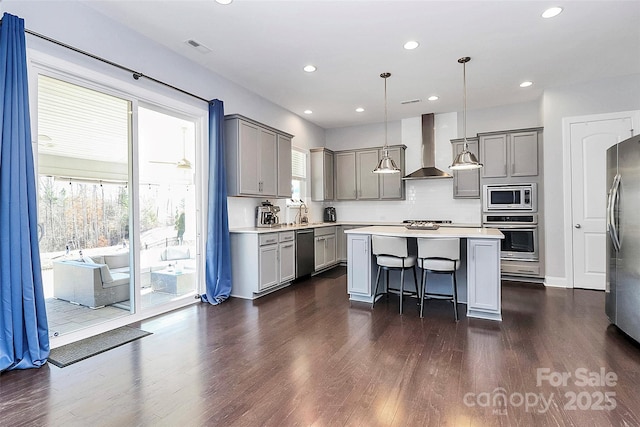 kitchen featuring wall chimney exhaust hood, a center island, hanging light fixtures, a kitchen breakfast bar, and stainless steel appliances