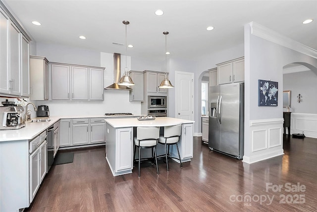 kitchen featuring gray cabinetry, stainless steel appliances, a center island, decorative light fixtures, and wall chimney exhaust hood