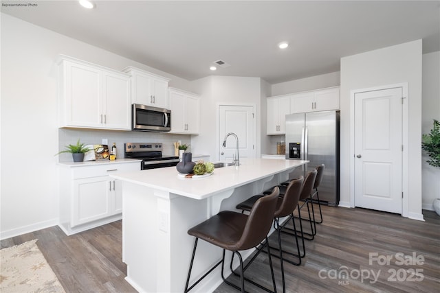 kitchen featuring a kitchen bar, sink, appliances with stainless steel finishes, a kitchen island with sink, and white cabinets