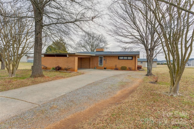 view of front of home featuring driveway, a chimney, and brick siding