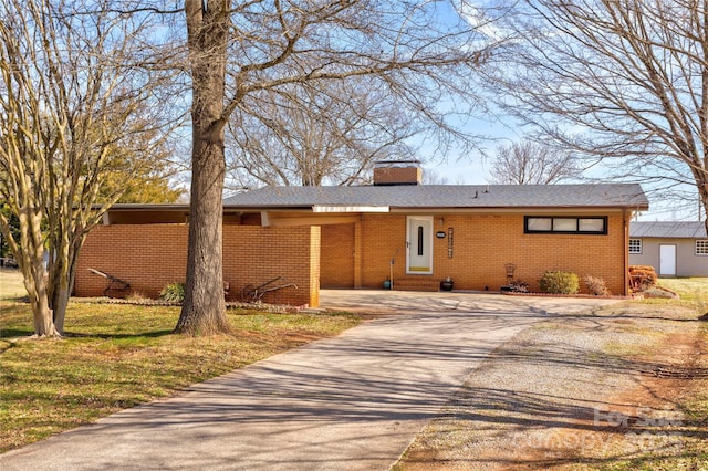 view of front facade with a front yard, brick siding, driveway, and a chimney