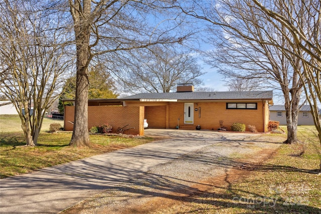 view of front of house with driveway, brick siding, a chimney, and a front yard