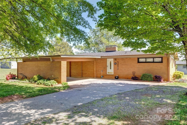 ranch-style house with an attached carport, driveway, a chimney, brick siding, and entry steps