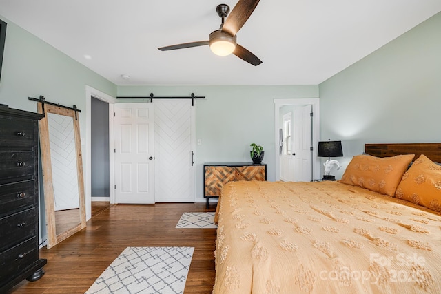 bedroom with ceiling fan, a barn door, and dark wood-type flooring