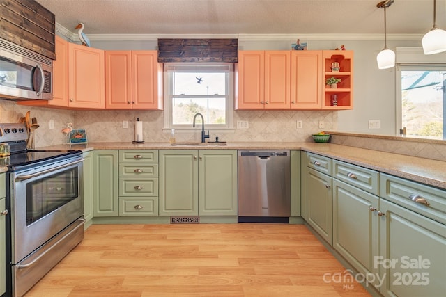 kitchen with sink, appliances with stainless steel finishes, hanging light fixtures, ornamental molding, and light wood-type flooring