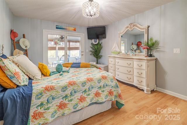 bedroom featuring an inviting chandelier, access to outside, a textured ceiling, and light wood-type flooring