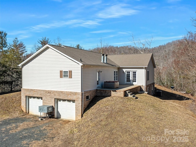 back of property featuring cooling unit, a garage, a hot tub, and a lawn