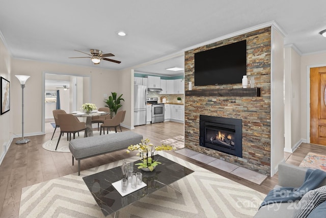 living room with crown molding, a stone fireplace, ceiling fan, and light hardwood / wood-style flooring