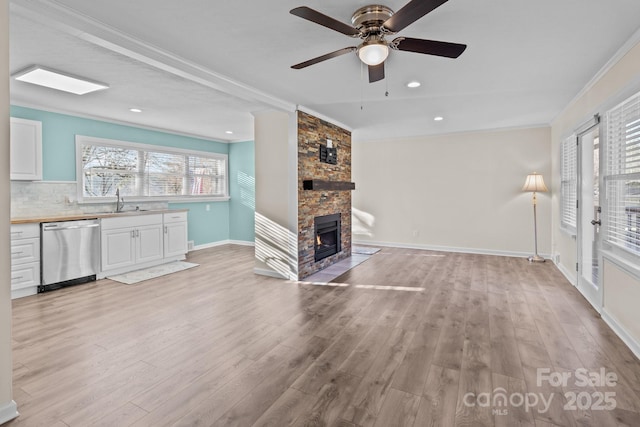 unfurnished living room with ornamental molding, sink, a fireplace, and light hardwood / wood-style flooring