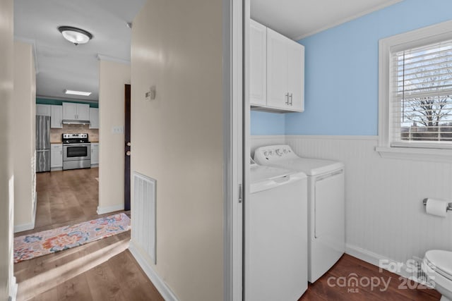 clothes washing area with dark wood-type flooring, ornamental molding, cabinets, and washing machine and clothes dryer