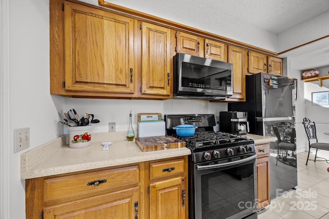 kitchen featuring light stone counters, stainless steel appliances, a textured ceiling, and light tile patterned floors