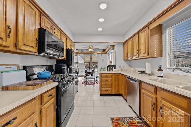 kitchen featuring sink, light tile patterned floors, black gas range oven, dishwasher, and ceiling fan