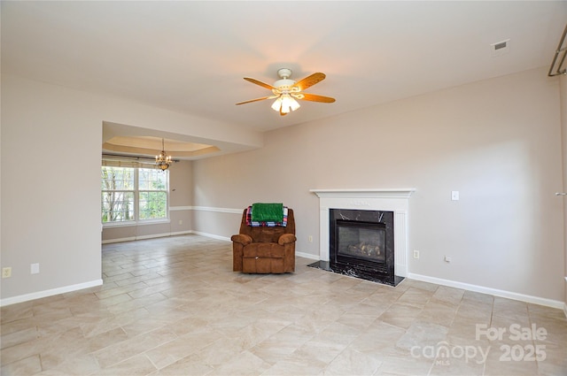 unfurnished room with visible vents, ceiling fan with notable chandelier, baseboards, a premium fireplace, and a raised ceiling