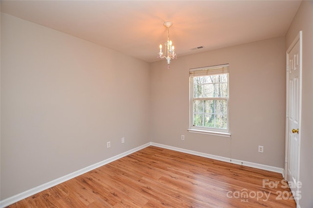 unfurnished room with visible vents, light wood-style flooring, an inviting chandelier, and baseboards