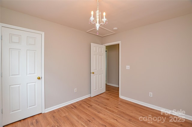 unfurnished bedroom featuring light wood finished floors, a notable chandelier, and baseboards