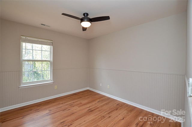 unfurnished room featuring visible vents, wainscoting, ceiling fan, and wood finished floors