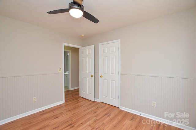 unfurnished bedroom with a wainscoted wall, a closet, a ceiling fan, and light wood finished floors