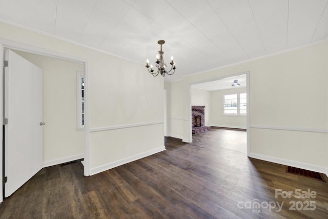 spare room with a notable chandelier, crown molding, a fireplace, and dark hardwood / wood-style flooring