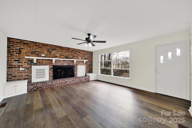 unfurnished living room with ceiling fan, brick wall, dark hardwood / wood-style floors, and a fireplace