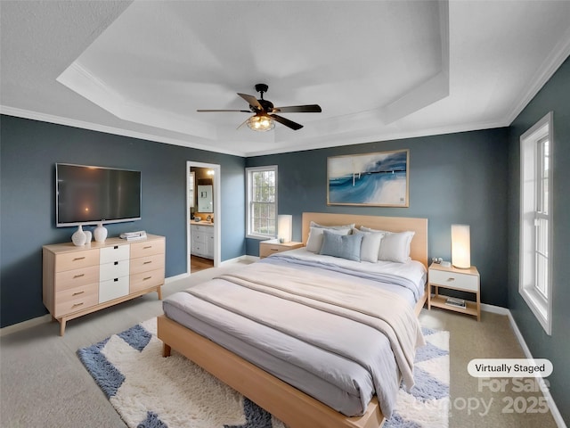 carpeted bedroom featuring ornamental molding, connected bathroom, ceiling fan, and a tray ceiling