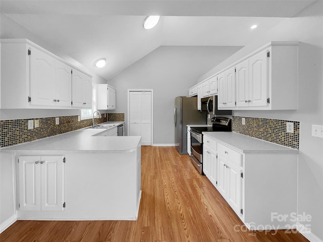 kitchen with lofted ceiling, sink, stainless steel appliances, white cabinets, and kitchen peninsula