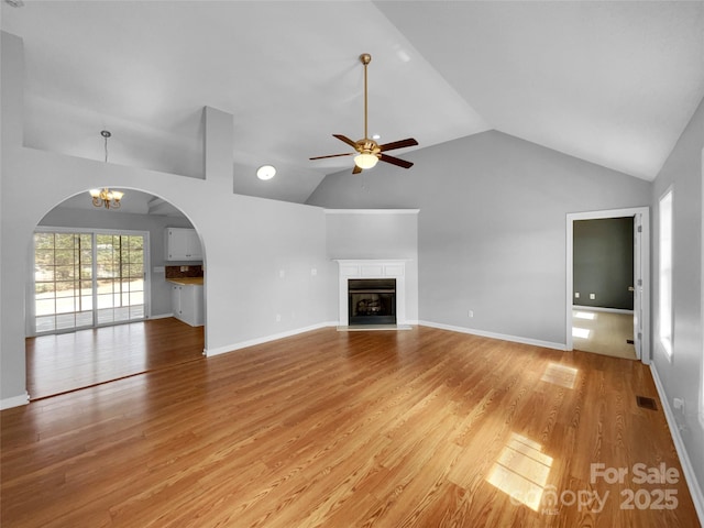 unfurnished living room with high vaulted ceiling, ceiling fan with notable chandelier, and light wood-type flooring