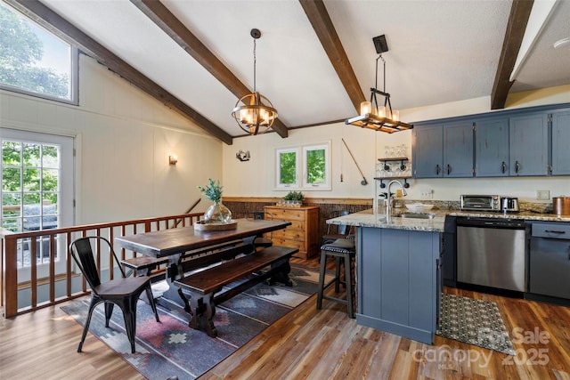 kitchen with blue cabinetry, sink, stainless steel dishwasher, pendant lighting, and light stone countertops