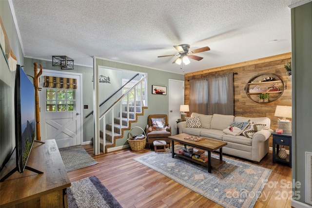 living room with hardwood / wood-style floors, crown molding, wooden walls, and a textured ceiling