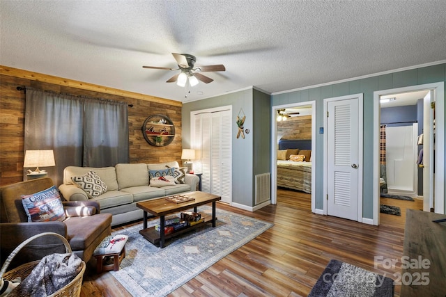 living room featuring ceiling fan, crown molding, wood-type flooring, and a textured ceiling