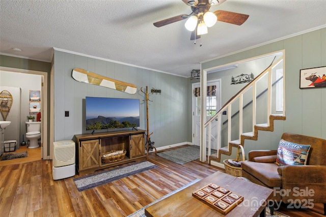 living room featuring ceiling fan, ornamental molding, wood-type flooring, and a textured ceiling