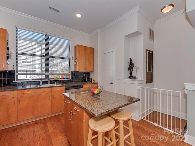 kitchen with ornamental molding, a center island, sink, and light wood-type flooring