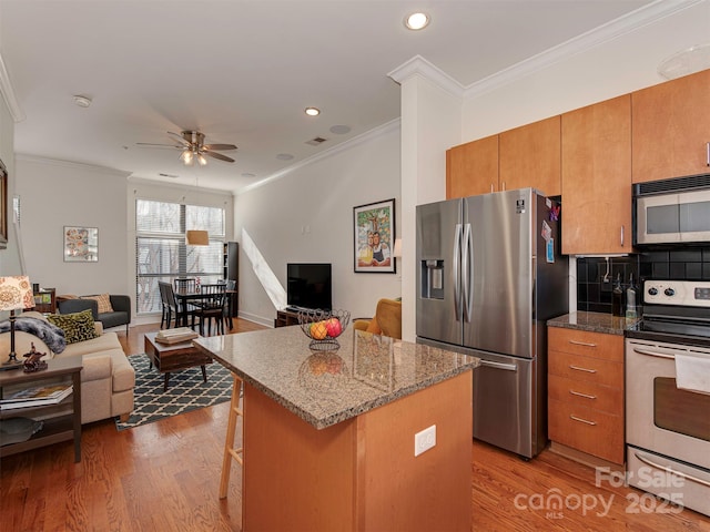 kitchen featuring crown molding, a kitchen bar, stainless steel appliances, a kitchen island, and light wood-type flooring