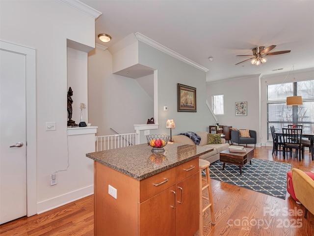 kitchen with a kitchen bar, crown molding, a center island, light wood-type flooring, and ceiling fan