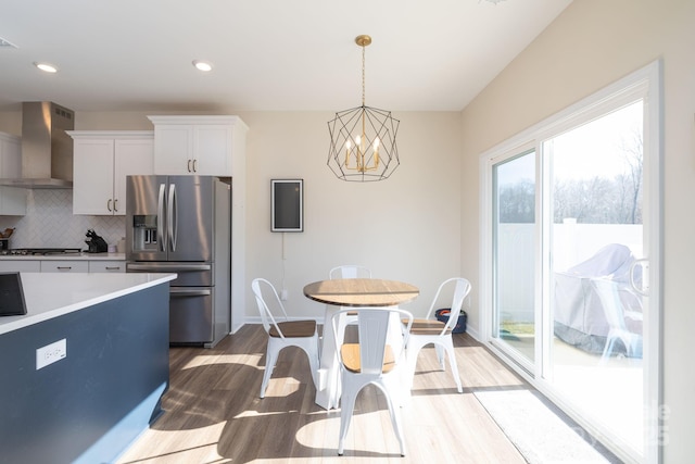 kitchen with hanging light fixtures, appliances with stainless steel finishes, white cabinets, wall chimney range hood, and backsplash