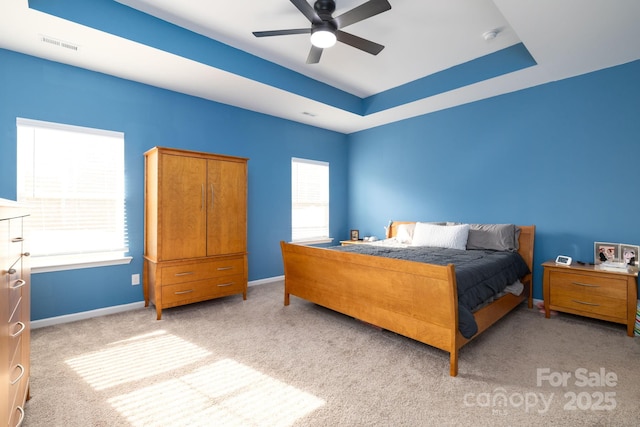 bedroom with ceiling fan, light colored carpet, a tray ceiling, and multiple windows