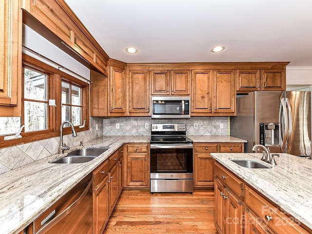 kitchen with light hardwood / wood-style floors, appliances with stainless steel finishes, light stone countertops, and sink