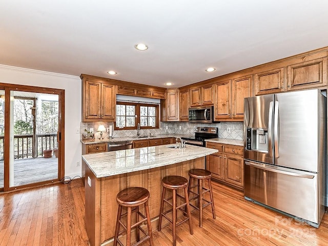 kitchen with sink, appliances with stainless steel finishes, a kitchen breakfast bar, light stone countertops, and a kitchen island