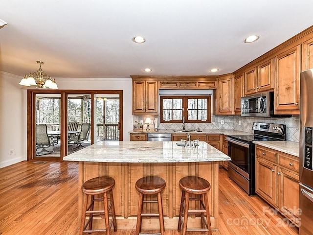 kitchen with sink, a kitchen breakfast bar, stainless steel appliances, light stone countertops, and a center island with sink