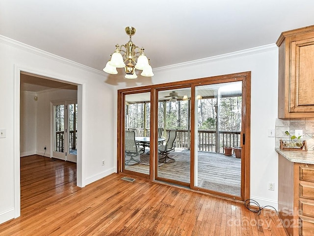 doorway with crown molding, a healthy amount of sunlight, a notable chandelier, and light hardwood / wood-style floors