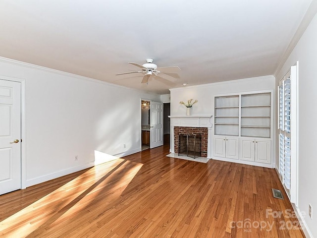 unfurnished living room featuring a brick fireplace, crown molding, hardwood / wood-style floors, and ceiling fan